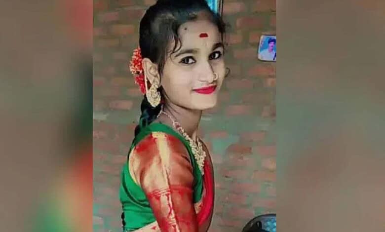 Young girl dressed in colourful traditional clothes, smiling, with a brick wall background.
