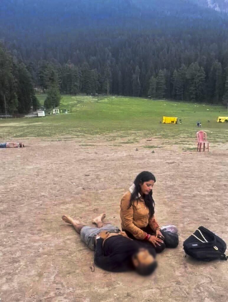Mountain landscape with a woman sitting on the ground and a person lying down nearby.
