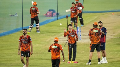 Cricket players in Hyderabad IPL match practice, wearing orange jerseys, preparing on the field amid weat.