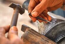 Close-up of artisan carving intricate designs on Bidriware metal vessel.