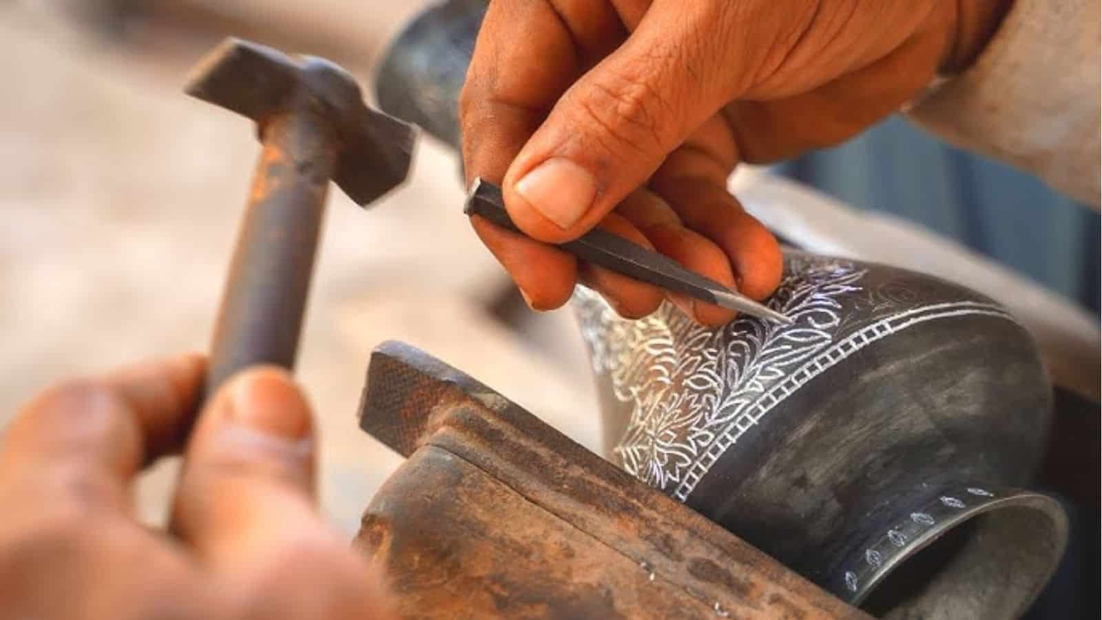 Close-up of artisan carving intricate designs on Bidriware metal vessel.