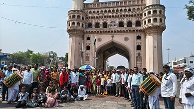 Crowds celebrating a tribal festival at Charminar with traditional music and dance.