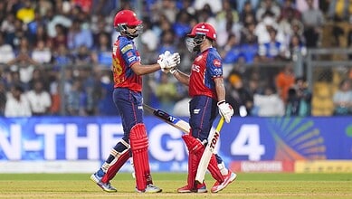 Two cricket players in red and blue uniforms celebrating after a successful play.