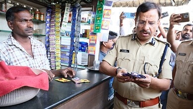 Shopkeeper and police officer examining items at a busy market stall in India.