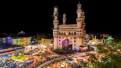 Adivasis experiencing city life in Hyderabad during the tour initiative, with the Charminar illuminated a.
