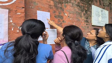 Group of students checking exam results posted on a brick wall, discussing the CBSE Class 12 results expe.