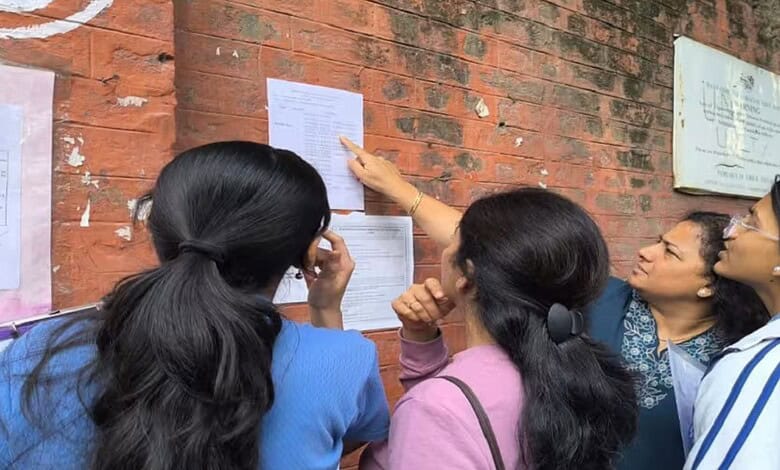 Group of students checking exam results posted on a brick wall, discussing the CBSE Class 12 results expe.