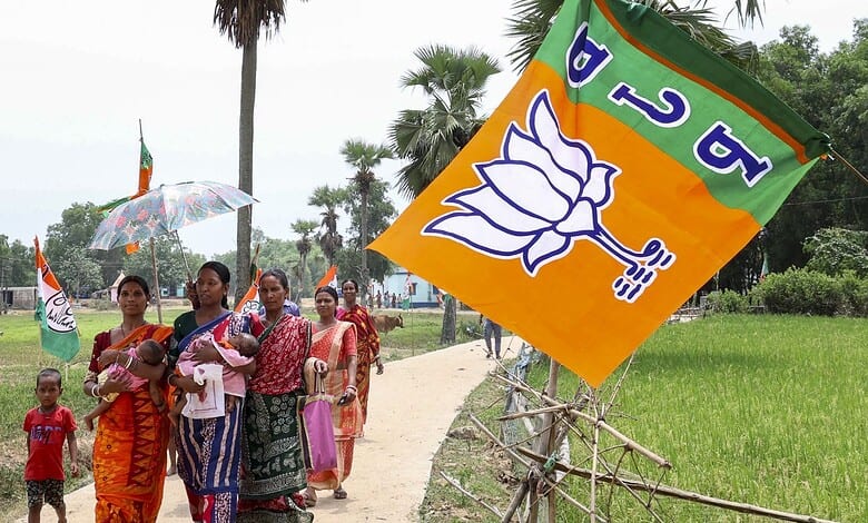 Women and children walking with BJP flags in a rural area during election campaign.