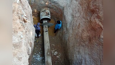 Workers inspecting a large pipe in a deep excavation site for infrastructure development.