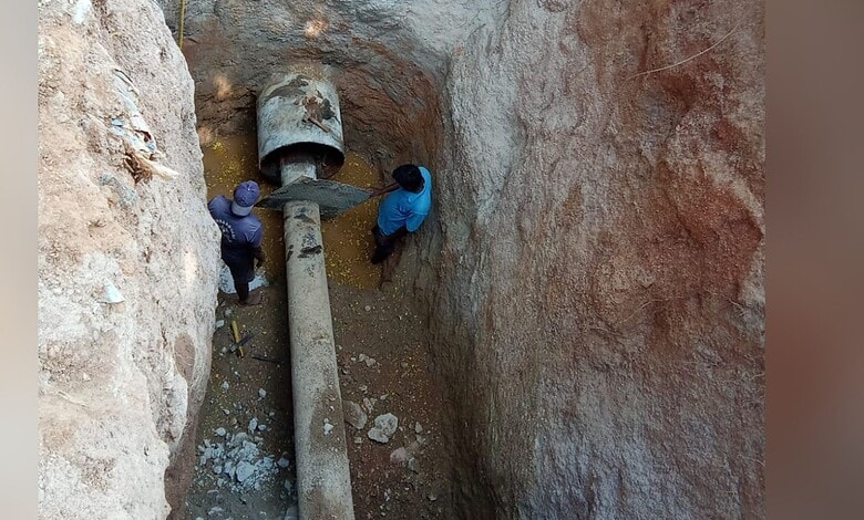 Workers inspecting a large pipe in a deep excavation site for infrastructure development.