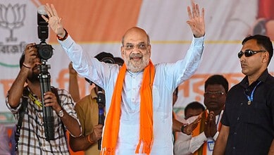Amit Shah waving to crowd during a political event, surrounded by supporters and media personnel.