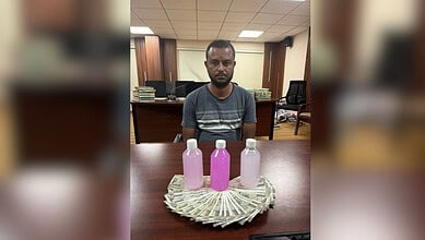 Man sitting at desk with three bottles of pink liquid and cash arranged in a fan shape in front of him.