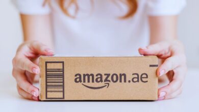 A person holding a cardboard Amazon.ae delivery package with a barcode on a white background.