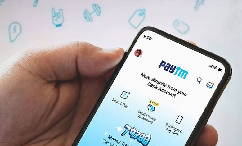 Close-up of a hand holding a smartphone displaying the Paytm app with banking options.