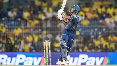 Cricket player in blue uniform batting during a match with a crowd in the background.