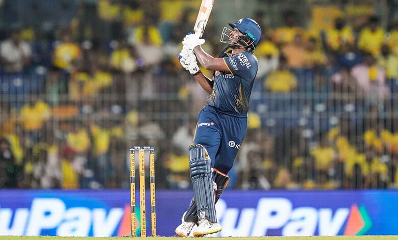 Cricket player in blue uniform batting during a match with a crowd in the background.