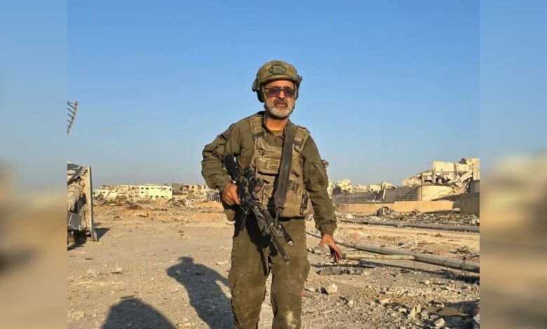 Israeli reservist rabbi Avraham Zerbiv standing in a war-damaged area of Gaza holding a rifle.