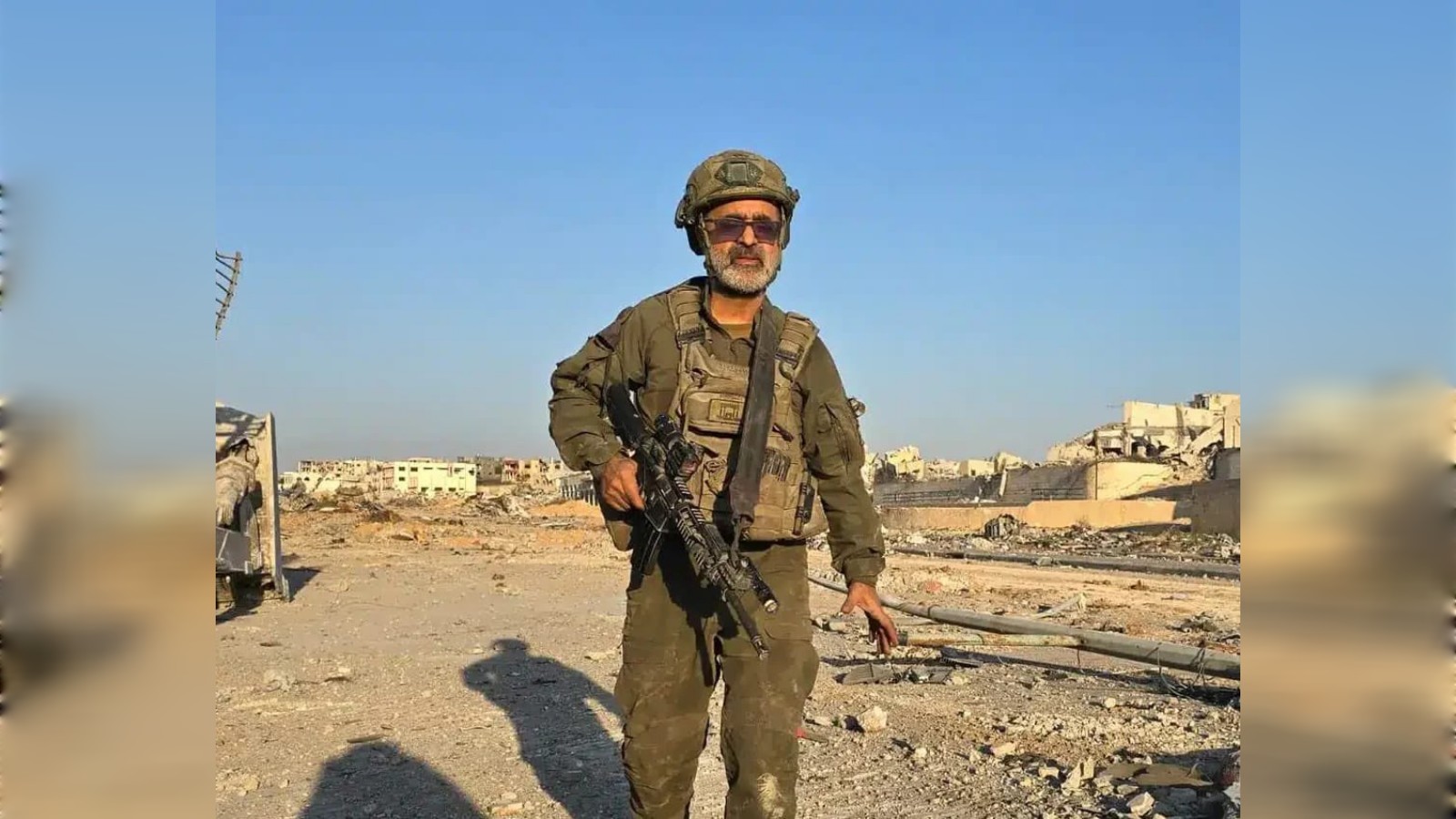 Israeli reservist rabbi Avraham Zerbiv standing in a war-damaged area of Gaza holding a rifle.