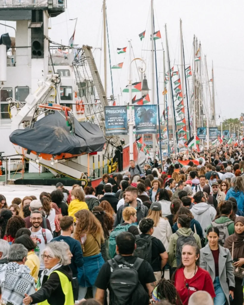 People crowd Barcelona port walkway as flotilla prepares to depart.