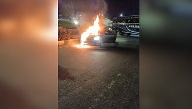 Car on fire causing traffic disruption at Narsingi TGPA rotary. Flames and smoke visible as emergency ser.