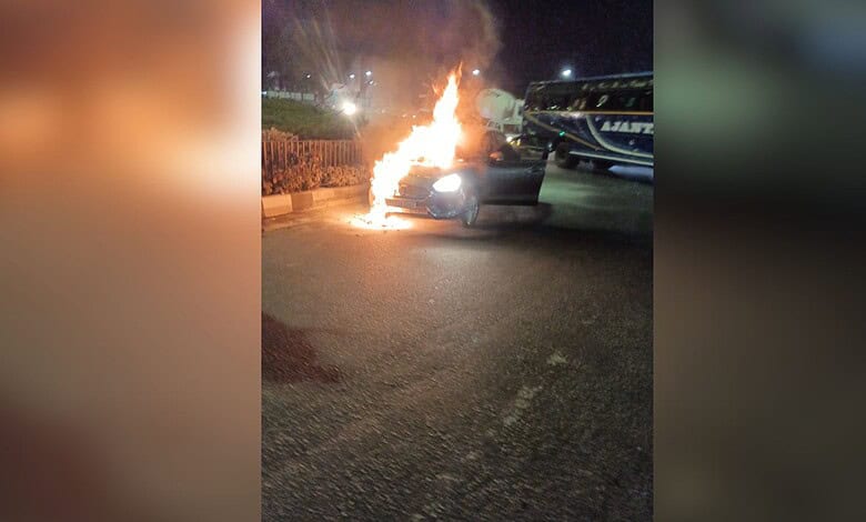 Car on fire causing traffic disruption at Narsingi TGPA rotary. Flames and smoke visible as emergency ser.