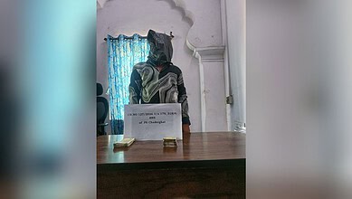 Person with face covered behind a desk with seized counterfeit currency notes, related to counterfeit cur.