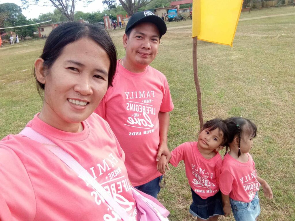 Filipino conjoined twins Klea and Maurice Ann stand with their parents outdoors before surgery, wearing matching pink shirts.