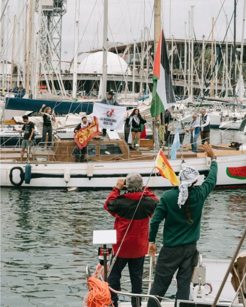 Activists on a small vessel wave Palestinian flags during flotilla departure.