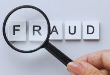 image shows A magnifying glass held over letter tiles spelling "FRAUD" on a light gray background.