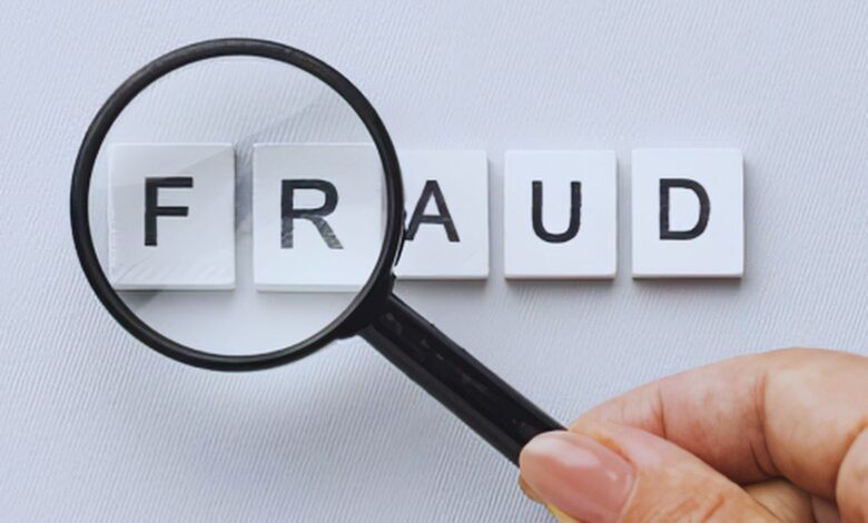 image shows A magnifying glass held over letter tiles spelling "FRAUD" on a light gray background.