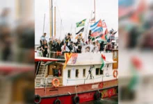 Activists wave flags aboard a flotilla vessel departing Barcelona port