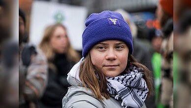 Young girl protester wearing a blue beanie and scarf at rally, surrounded by a crowd.