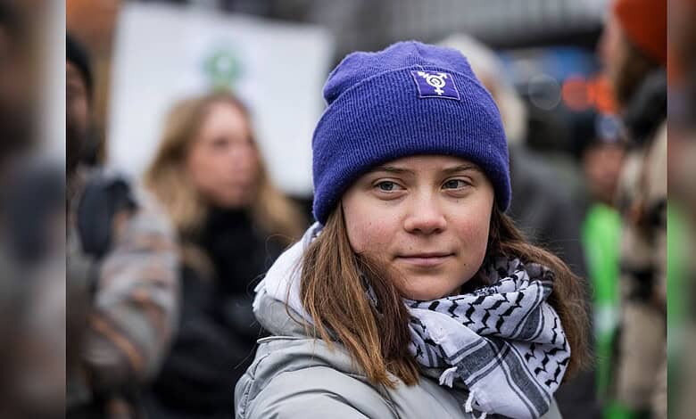 Young girl protester wearing a blue beanie and scarf at rally, surrounded by a crowd.