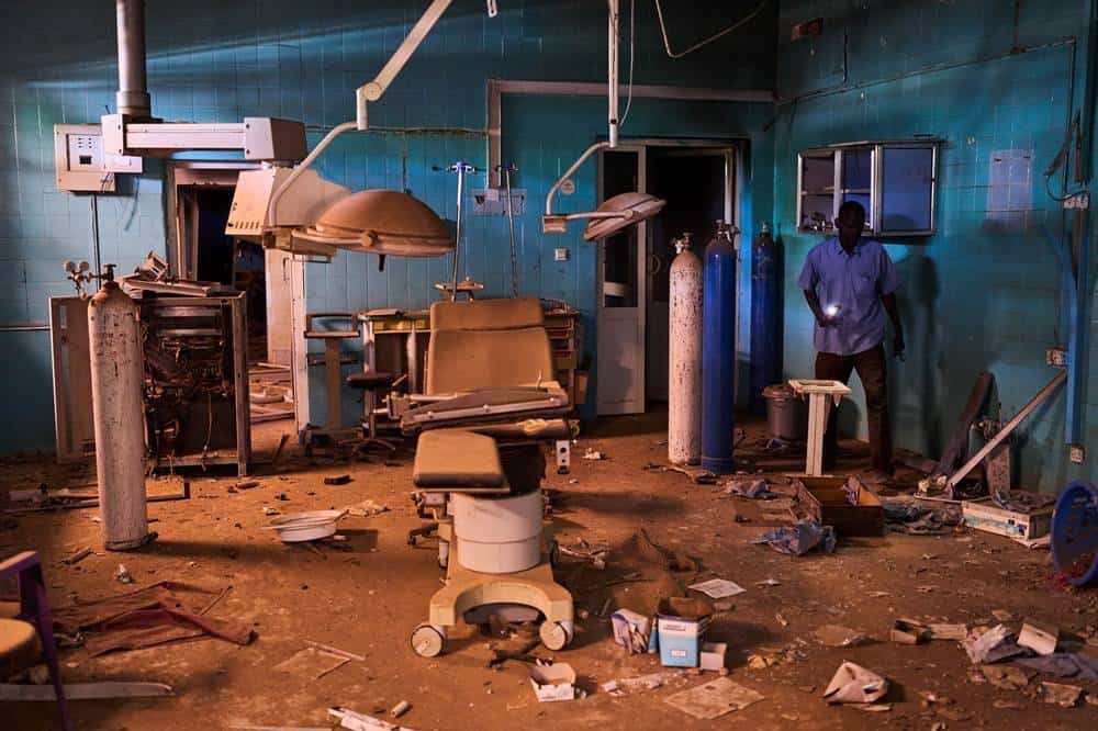 Abandoned hospital room with medical equipment and debris after conflict.