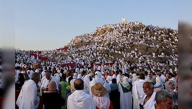 Pilgrims in white Ihram clothing gather at a hilltop during Hajj pilgrimage.
