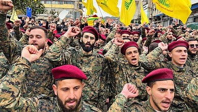 Hezbollah fighters in military uniform and red berets participate in a rally with yellow flags, showing r.