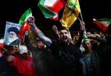 Protesters waving Iranian and Hezbollah flags and holding a portrait of Ayatollah Ali Khamenei during a night-time rally.