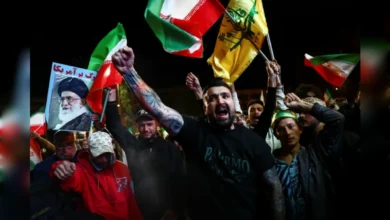 Protesters waving Iranian and Hezbollah flags and holding a portrait of Ayatollah Ali Khamenei during a night-time rally.