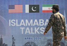 Soldier walks past Islamabad talks display with US, Pakistan and Iran flags.