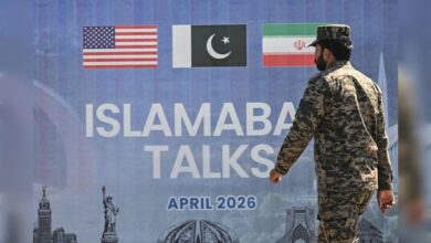 Soldier walks past Islamabad talks display with US, Pakistan and Iran flags.