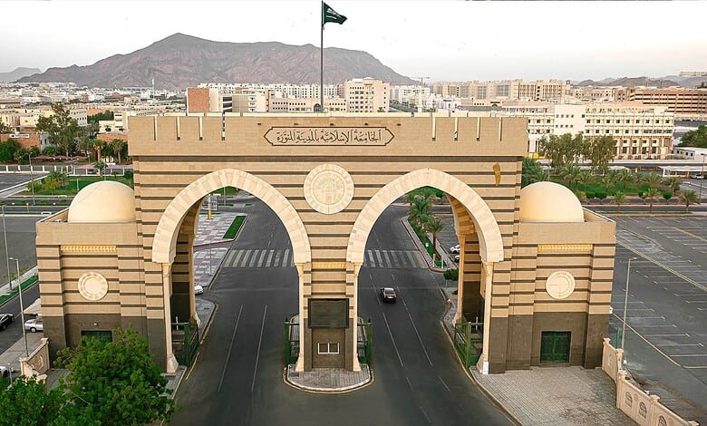 Main entrance gate of the Islamic University of Madinah with city skyline and mountains in the background.