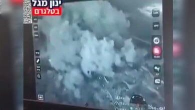 Thick smoke billows over rubble after a building is blown up in southern Lebanon, shown on a screen displaying circulated video footage.