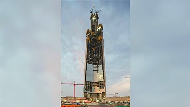 Skyscraper under construction in an urban area with cranes and scaffolding, part of a city skyline.