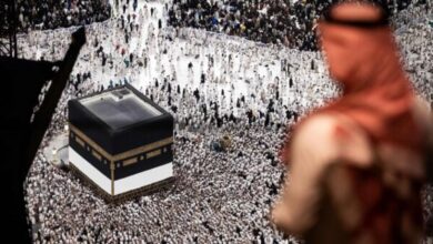 Muslim pilgrims gathered around the Kaaba at the Grand Mosque in Makkah, with a blurred figure in the foreground.