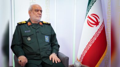 Majid Khademi seated in military uniform beside Iranian flag.