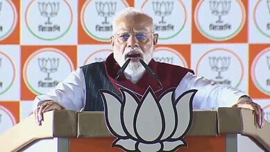 Indian Prime Minister Narendra Modi speaking at a political rally with BJP symbols in the background.