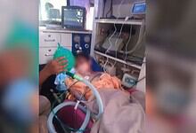 Boy in hospital bed with medical equipment and monitors, receiving oxygen therapy after balcony fall inci.