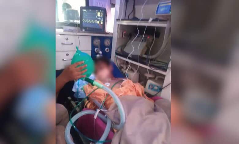 Boy in hospital bed with medical equipment and monitors, receiving oxygen therapy after balcony fall inci.