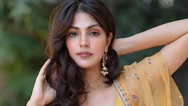 Rhea Chakraborty in a yellow traditional outfit, posing outdoors with greenery in the background.