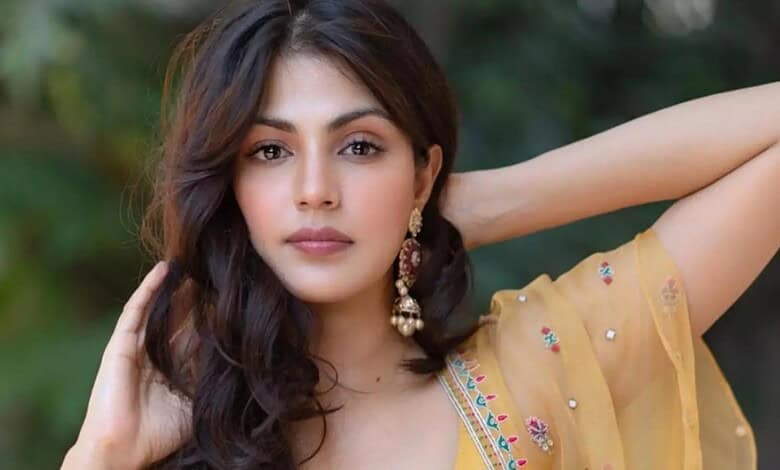 Rhea Chakraborty in a yellow traditional outfit, posing outdoors with greenery in the background.
